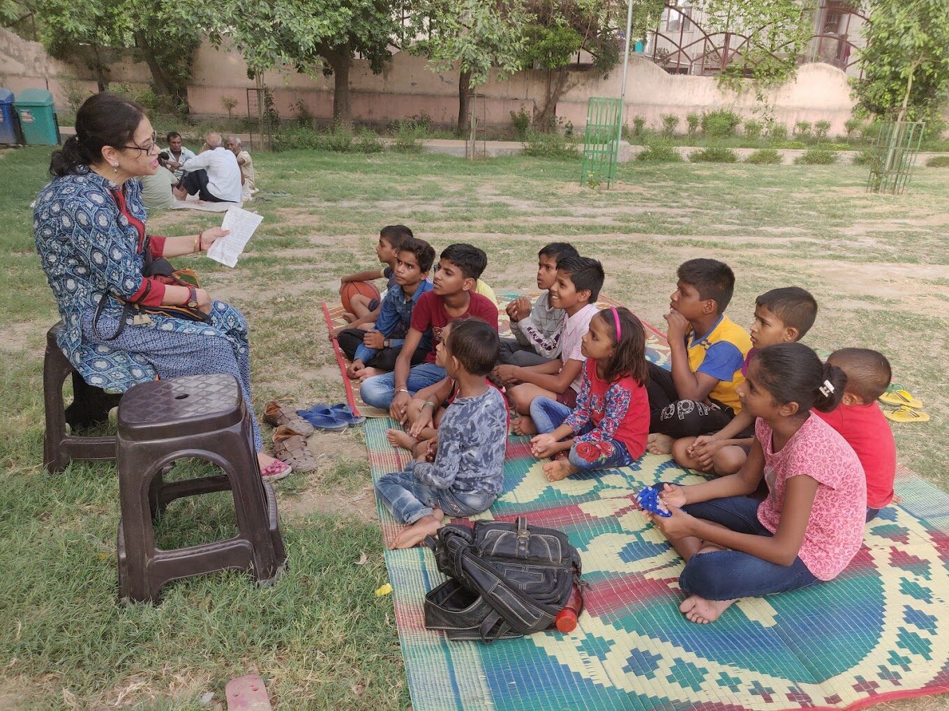 SVSPF mentor reading a story to a group of underprivileged children seated on a mat in a park